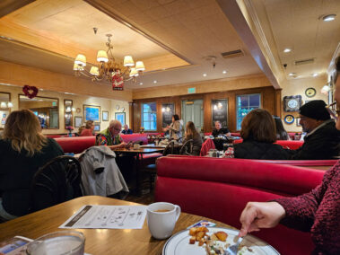 Wide picture of people in a restaurant and lady speaking in front of the group.