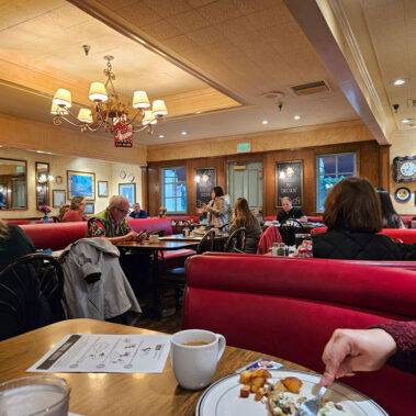 Wide picture of people in a restaurant and lady speaking in front of the group.